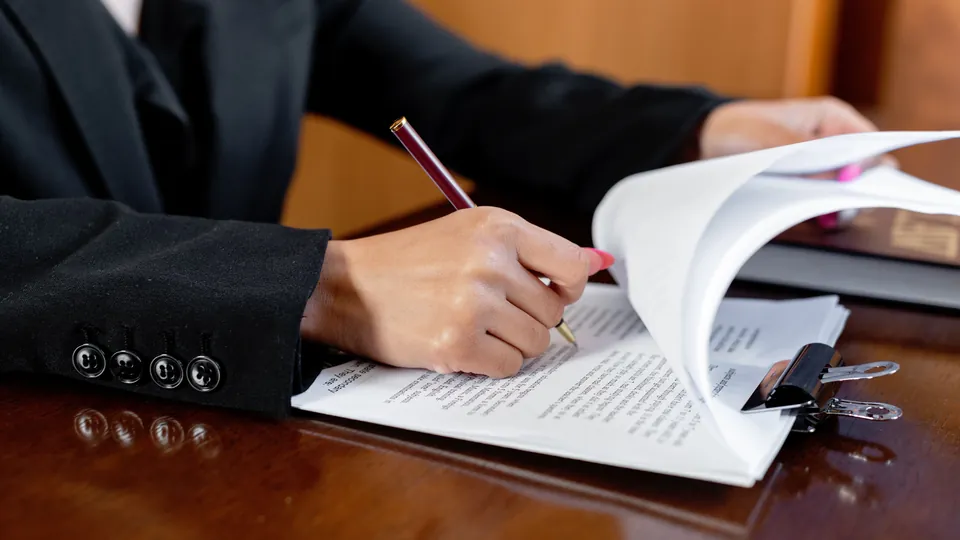 Close-up of a person writing on a document with a pen.