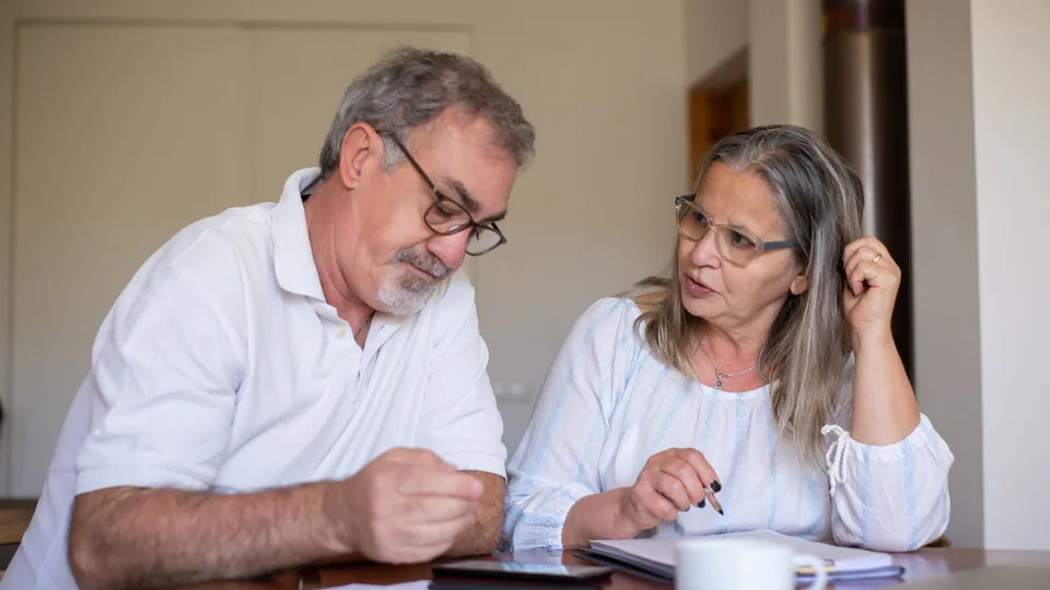 Older couple reviewing and completing documents together at a table.