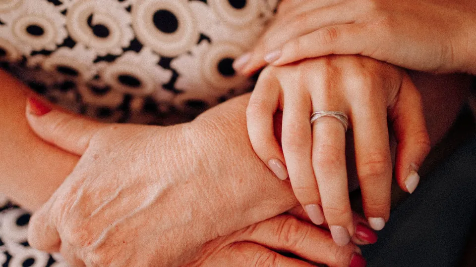 Close-up of an adult daughter holding her mother’s hands.