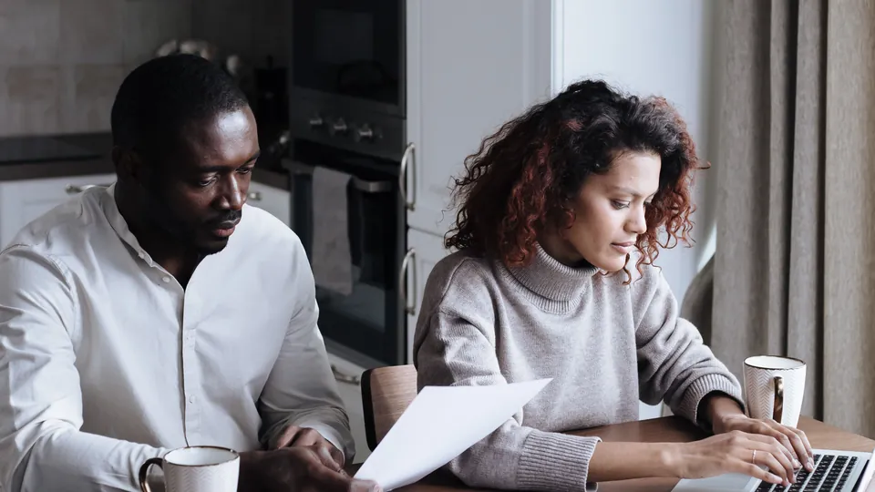 Couple reviewing papers and a laptop together at their kitchen table.