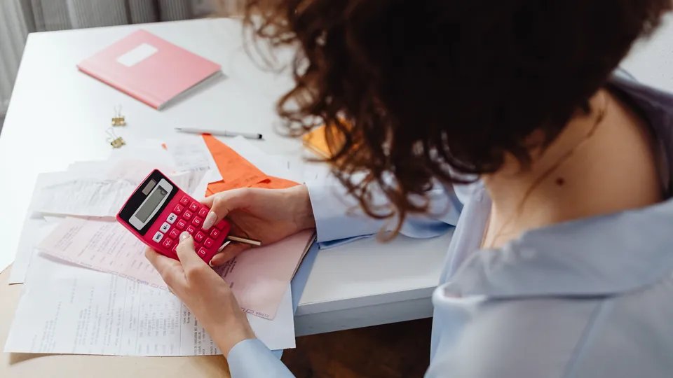 Woman reviewing paperwork with a calculator at her desk.